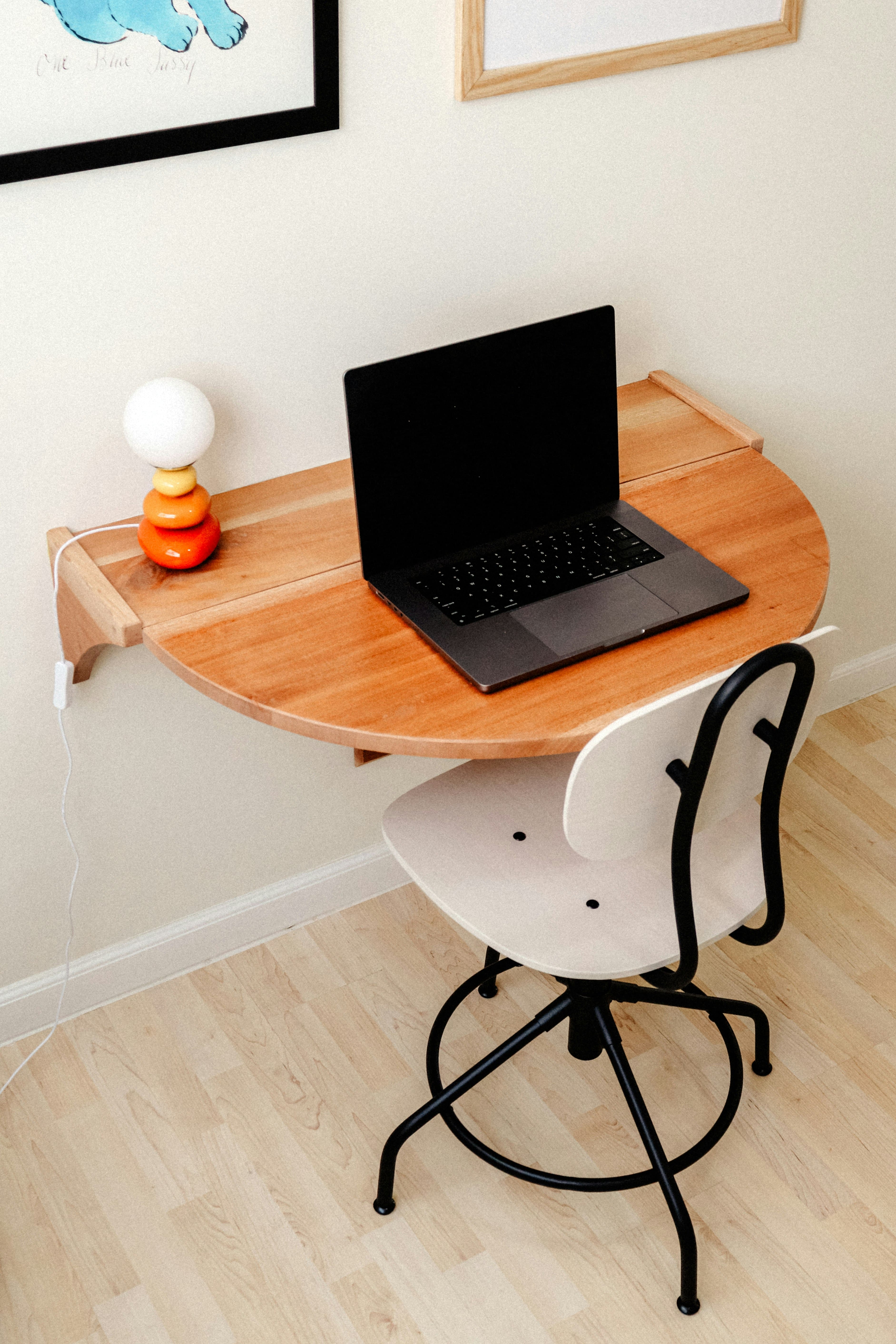 Home office compacto com bancada suspensa de madeira, notebook e cadeira branca