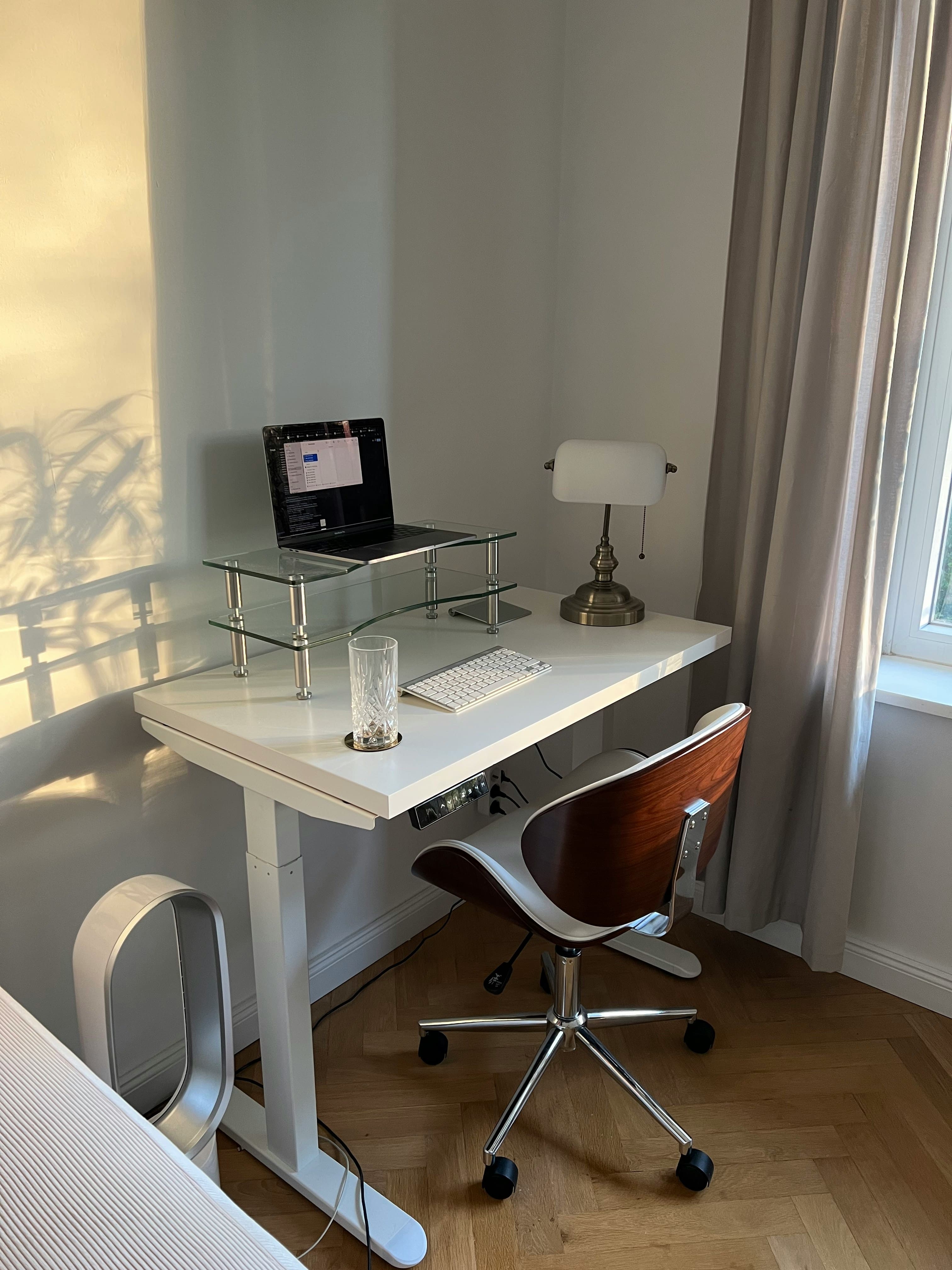 Escrivaninha de vidro com notebook e cadeira junto à janela com cortina