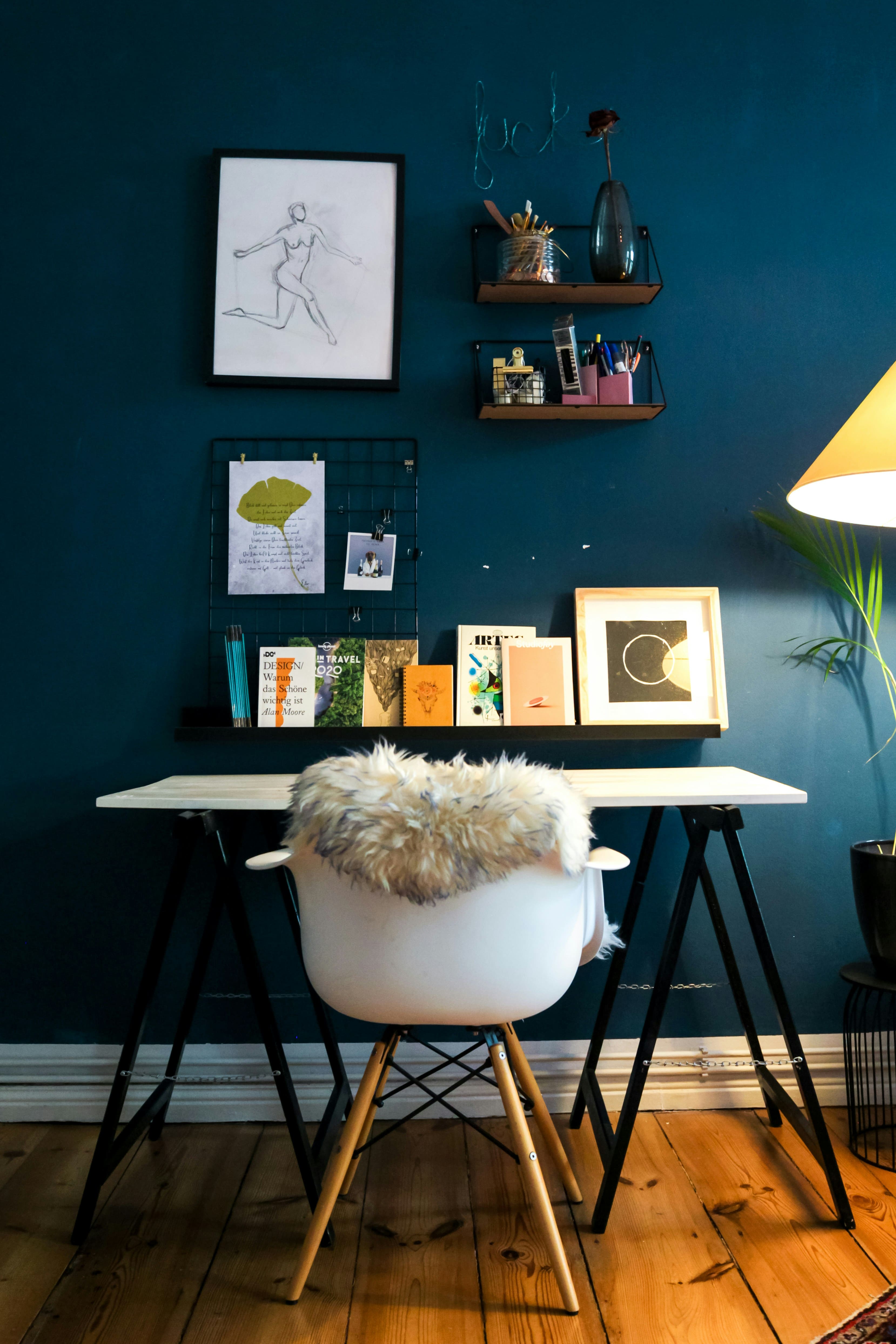 Home office com parede azul, escrivaninha branca e prateleiras com objetos