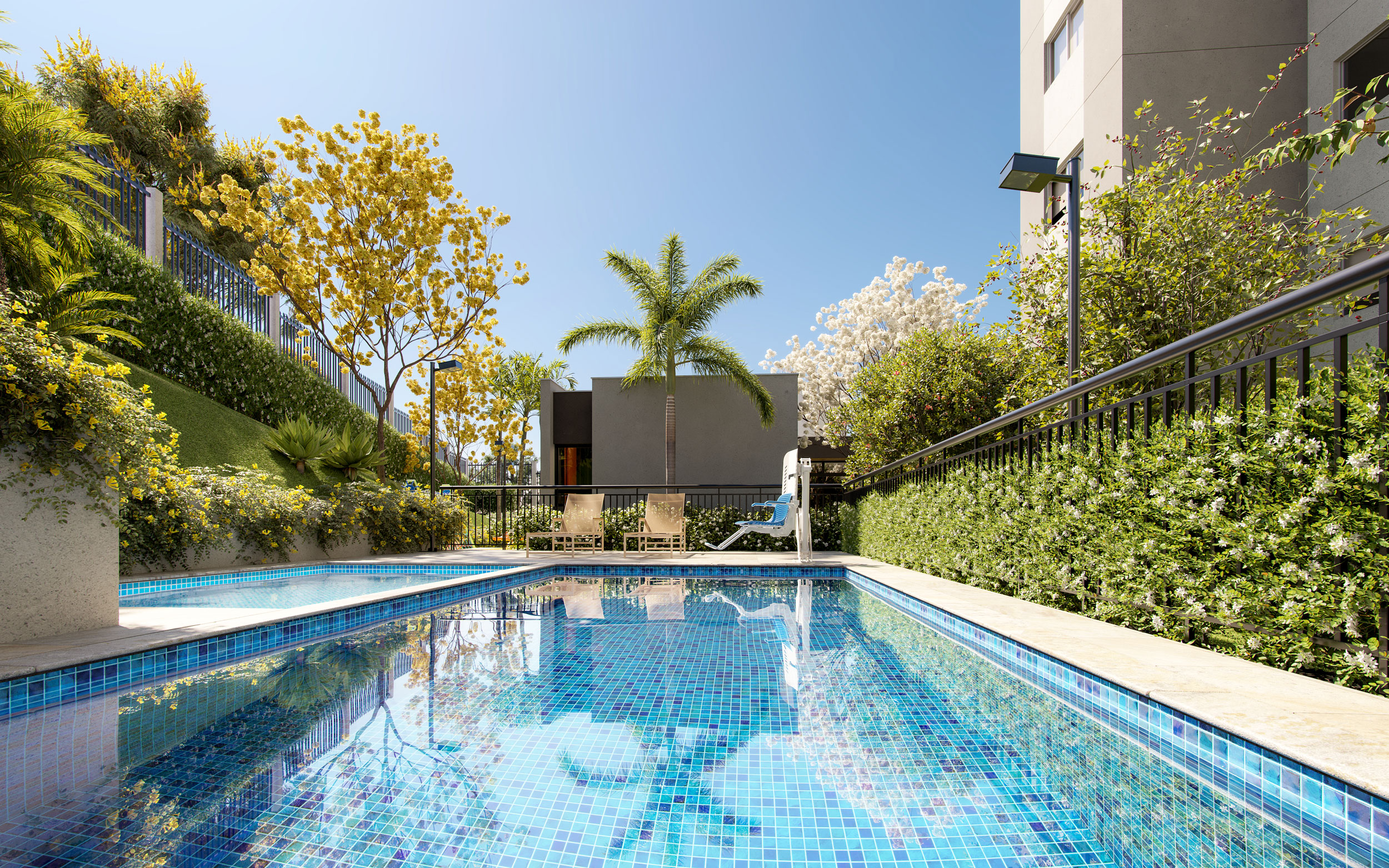 Piscina do condomínio cercada por deck e jardim, com o edifício ao fundo