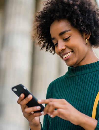 Mulher sorrindo enquanto usa o celular em ambiente interno iluminado